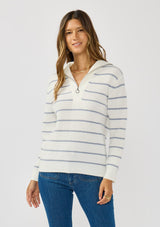 [Color: White/Blue] A front facing image of a brunette model wearing a white and blue striped knit pullover sweater with a half zip front. 