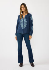 [Color: Navy] A front facing image of a brunette model wearing a blue embroidered blouse with a button front and long sleeves with button cuffs. A boho blouse for the fall season. 