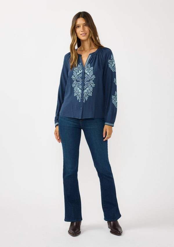[Color: Navy] A front facing image of a brunette model wearing a blue embroidered blouse with a button front and long sleeves with button cuffs. A boho blouse for the fall season. 