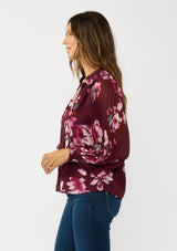 [Color: Wine/Dusty Rose] A side facing image a brunette model wearing a burgundy floral blouse with long voluminous pleated sleeves, split v-neckline, and a hidden button front. Perfect for the office, holidays, or other special occasions. 