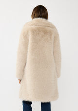 [Color: Sand] A back facing image of a brunette model wearing a beige faux fur coat with a shawl collared neckline, and side pockets. A large fur coat for the winter, holidays, and other special occasions. 