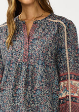 [Color: Navy/Rose] A detail image of a brunette model wearing a navy floral border print blouse with a button front and long sleeves with lace trim accents.