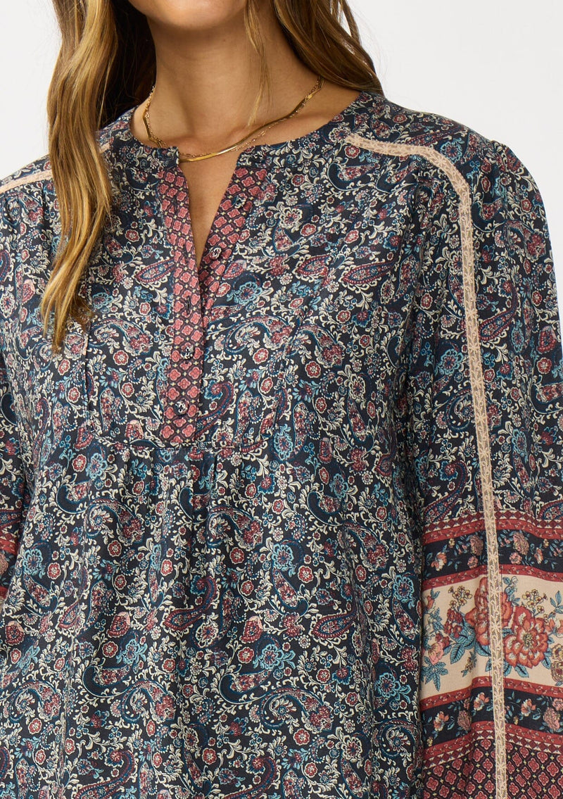 [Color: Navy/Rose] A detail image of a brunette model wearing a navy floral border print blouse with a button front and long sleeves with lace trim accents.
