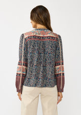 [Color: Navy/Rose] A back facing image of a brunette model wearing a navy floral border print blouse with a button front and long sleeves with lace trim accents.