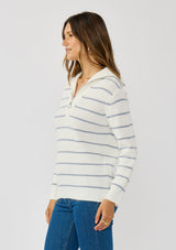 [Color: White/Blue] A side facing image of a brunette model wearing a white and blue striped knit pullover sweater with a half zip front. 