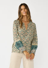 [Color: Taupe/Dusty Teal] A front facing image of a brunette model wearing a green teal floral blouse with a split v-neckline, lace accent on sleeves, and ruffled elastic cuffs. A fall boho blouse for casual styling. 