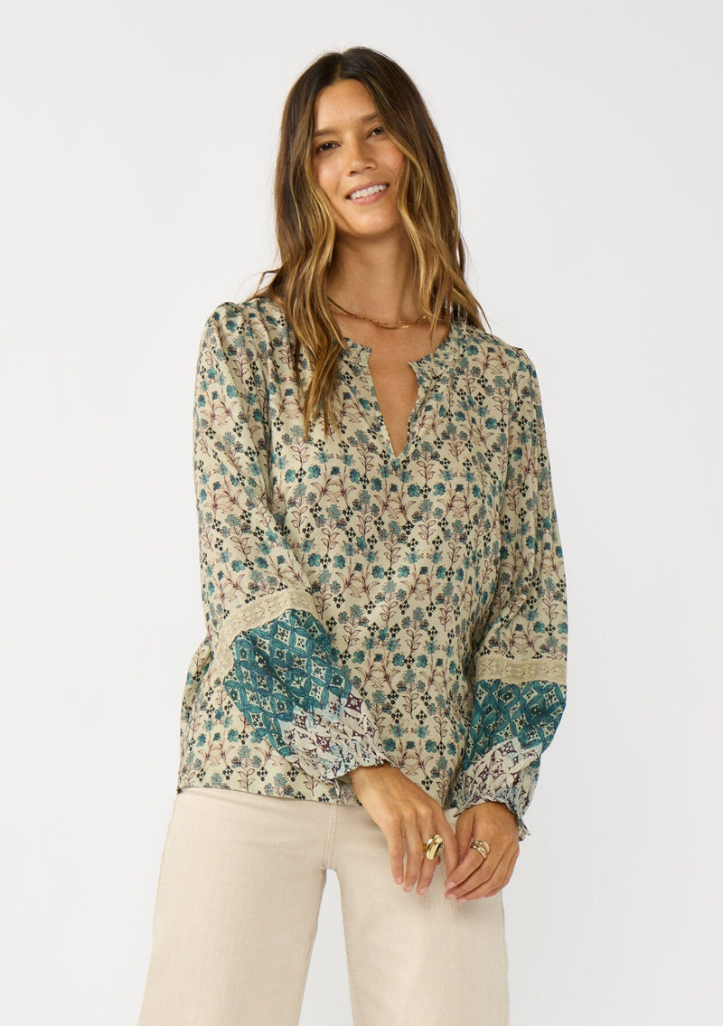 [Color: Taupe/Dusty Teal] A front facing image of a brunette model wearing a green teal floral blouse with a split v-neckline, lace accent on sleeves, and ruffled elastic cuffs. A fall boho blouse for casual styling. 