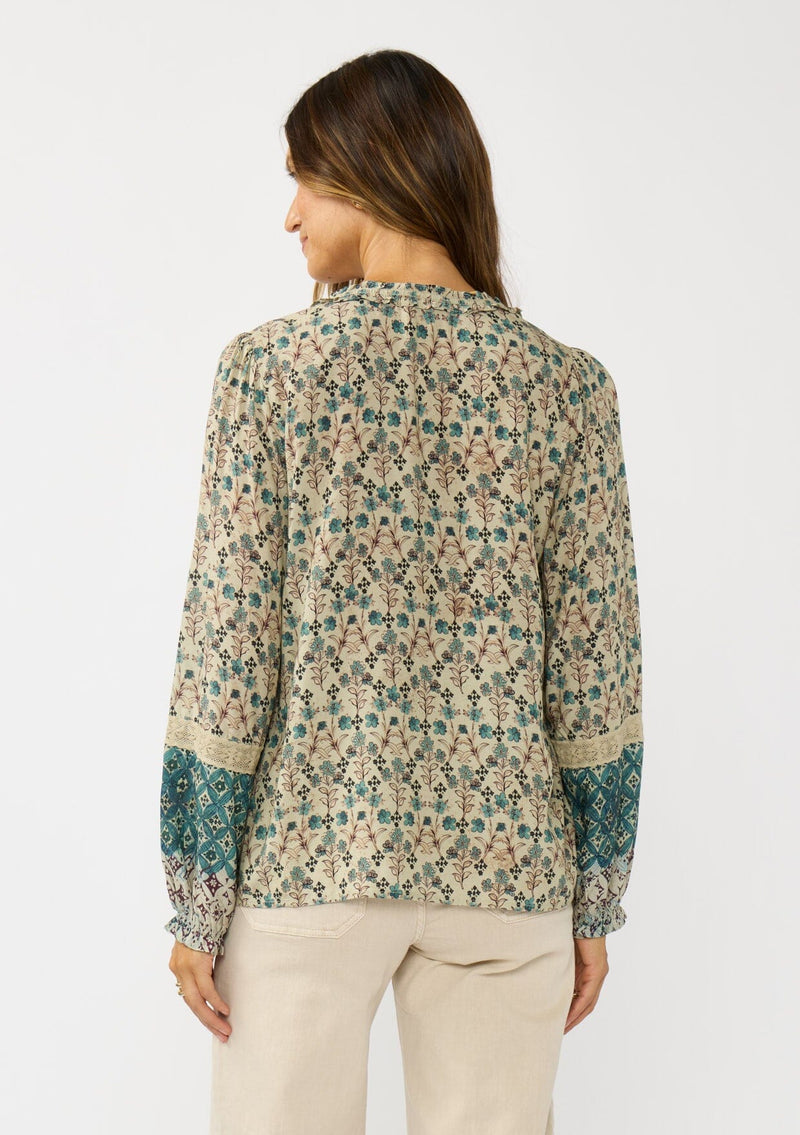 [Color: Taupe/Dusty Teal] A back facing image of a brunette model wearing a green teal floral blouse with a split v-neckline, lace accent on sleeves, and ruffled elastic cuffs. A fall boho blouse for casual styling. 