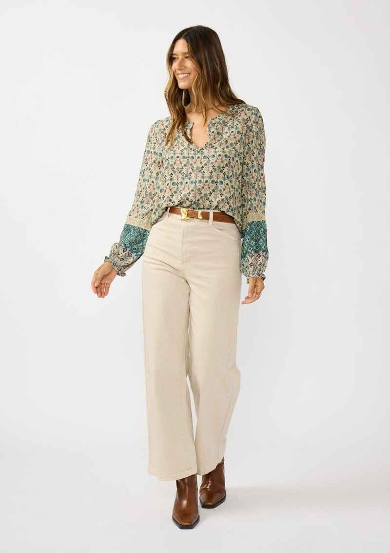 [Color: Taupe/Dusty Teal] A front facing image of a brunette model wearing a green teal floral blouse with a split v-neckline, lace accent on sleeves, and ruffled elastic cuffs. A fall boho blouse for casual styling. 