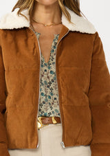 [Color: Camel] A detail image of a brunette model wearing a brown corduroy puffer jacket with a sherpa collar, zip-up front, and welt pockets. 