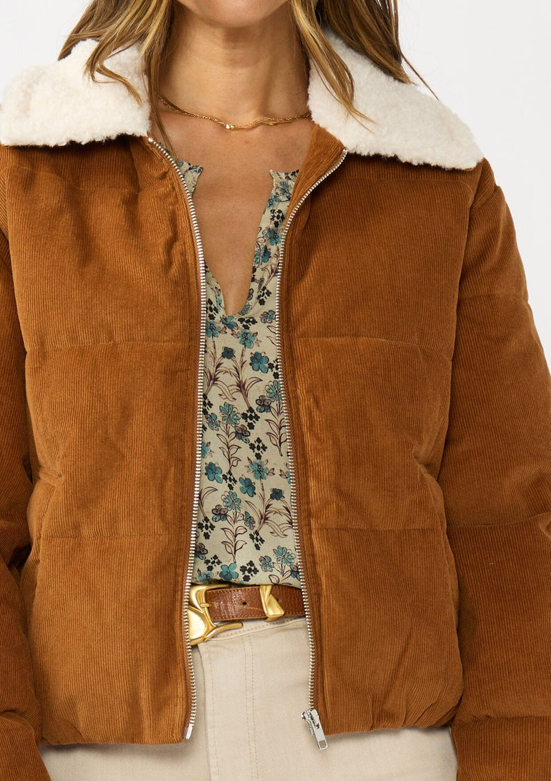 [Color: Camel] A detail image of a brunette model wearing a brown corduroy puffer jacket with a sherpa collar, zip-up front, and welt pockets. 