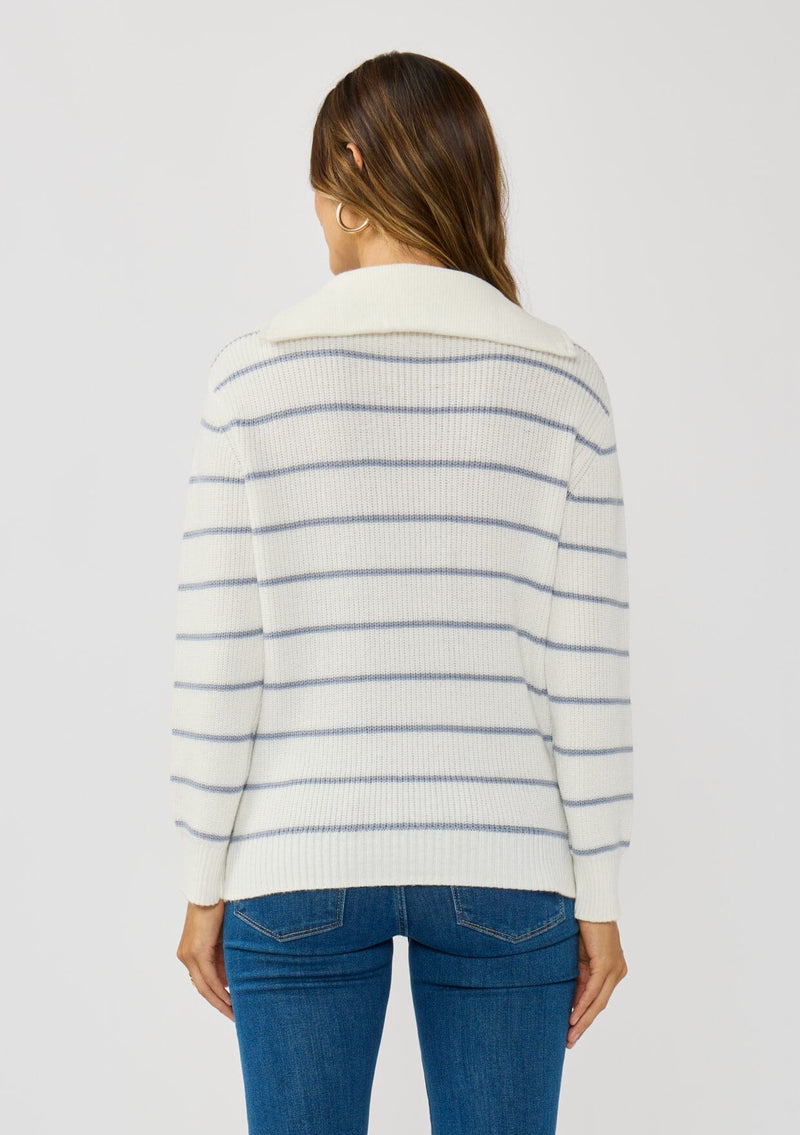 [Color: White/Blue] A back facing image of a brunette model wearing a white and blue striped knit pullover sweater with a half zip front. 