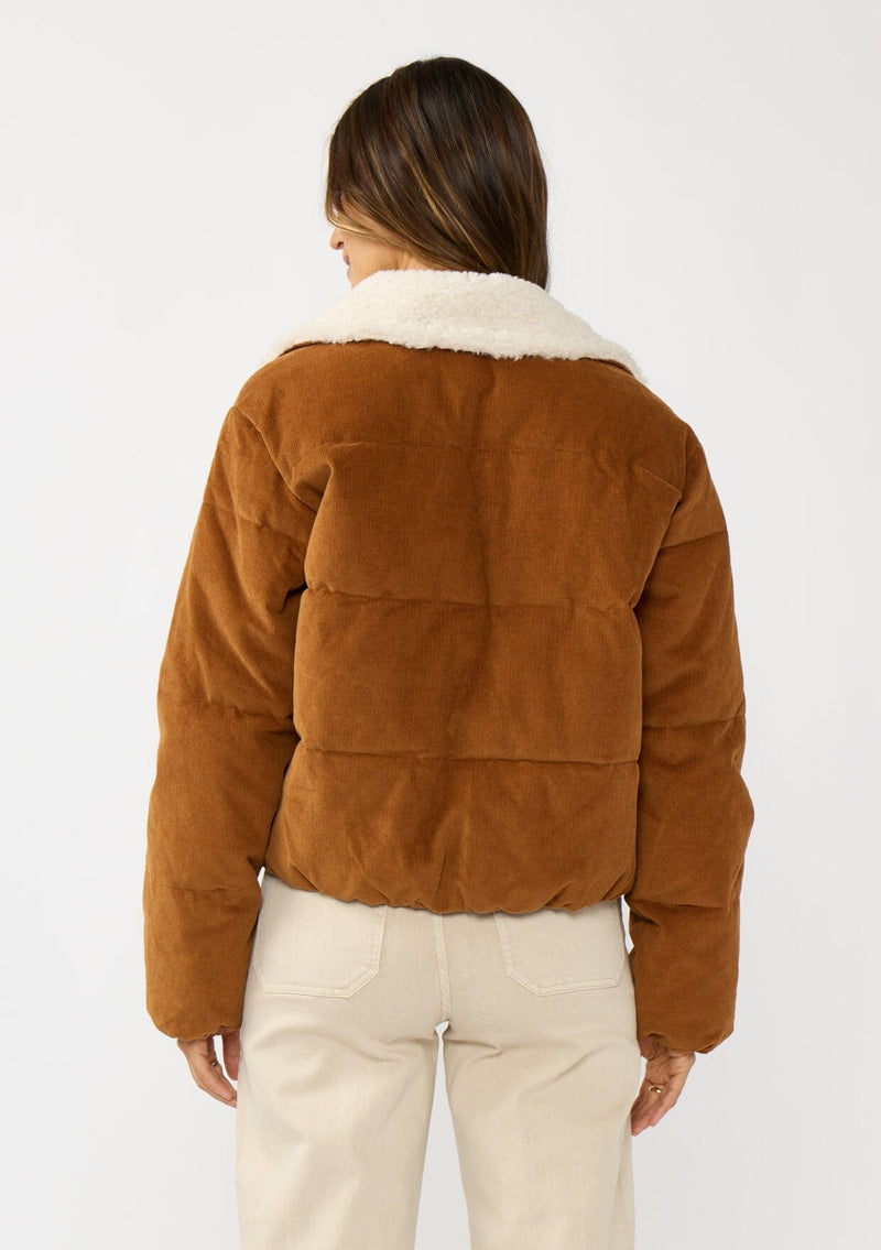 [Color: Camel] A back facing image of a brunette model wearing a brown corduroy puffer jacket with a sherpa collar, zip-up front, and welt pockets. 