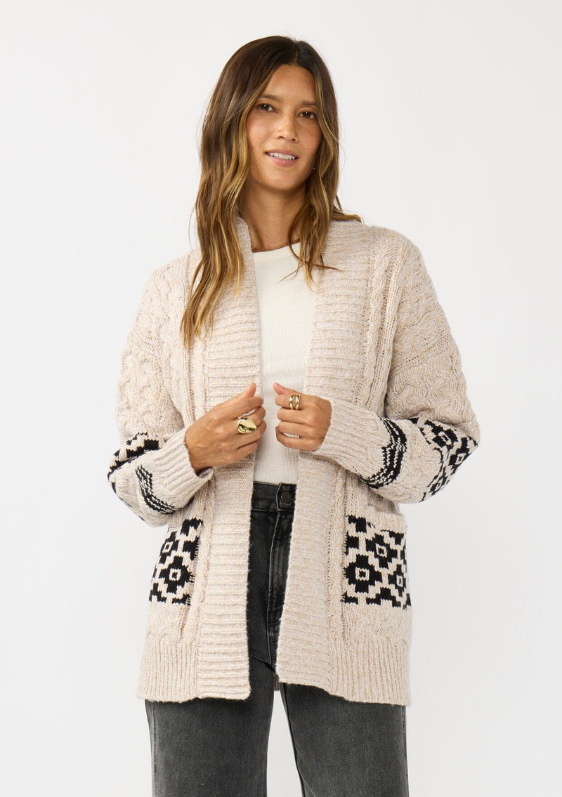 [Color: Natural/Black] A front facing image of a brunette model wearing a marled knit cardigan with a trendy diamond pattern, an open front, and ribbed border. A southwestern inspired knit cardigan with a boho relaxed fit. 