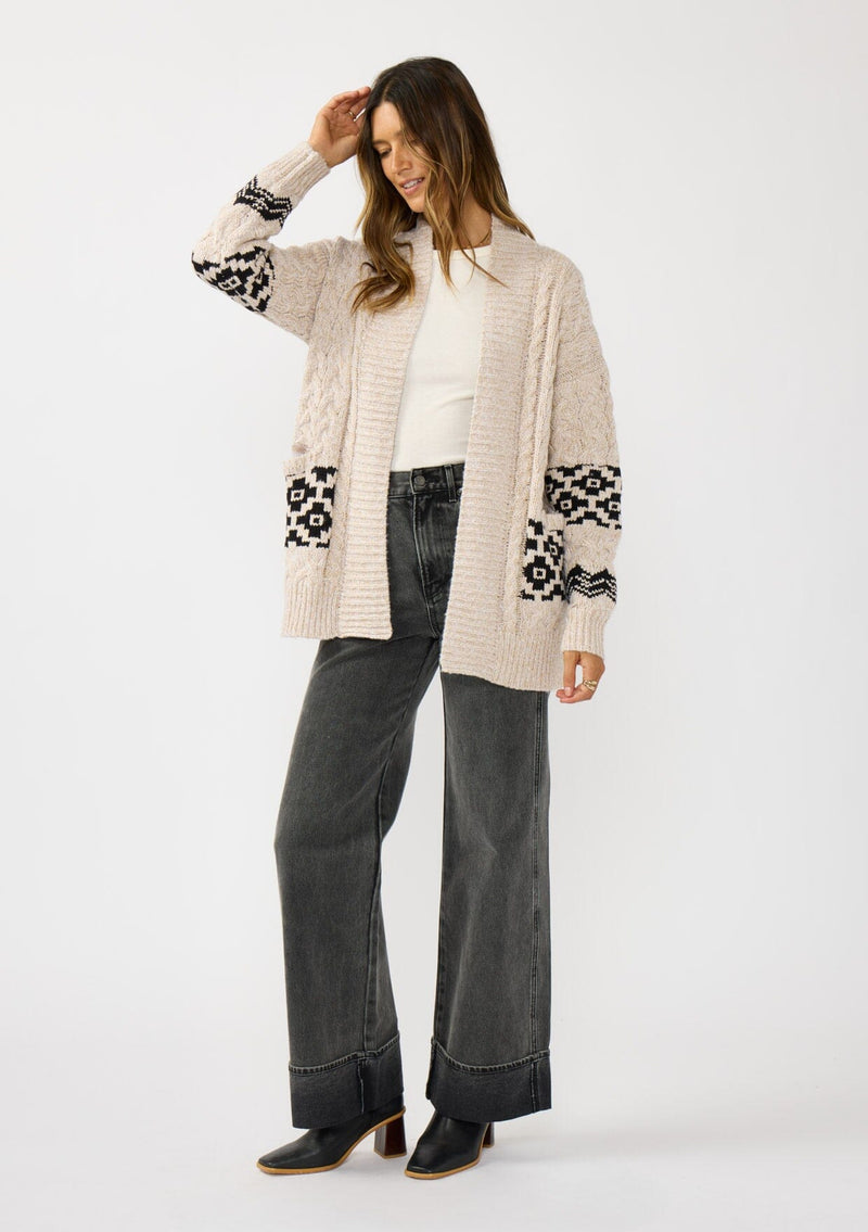 [Color: Natural/Black] A front facing image of a brunette model wearing a marled knit cardigan with a trendy diamond pattern, an open front, and ribbed border. A southwestern inspired knit cardigan with a boho relaxed fit. 