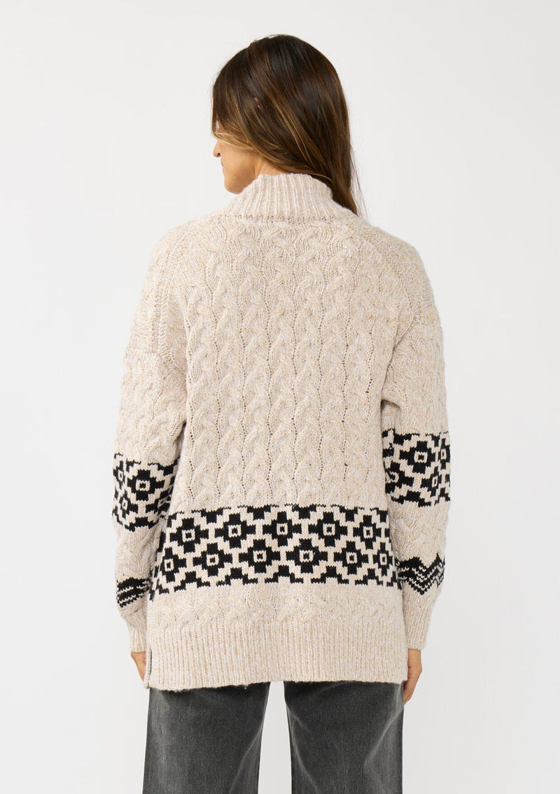 [Color: Natural/Black] A back facing image of a brunette model wearing a marled knit cardigan with a trendy diamond pattern, an open front, and ribbed border. A southwestern inspired knit cardigan with a boho relaxed fit. 