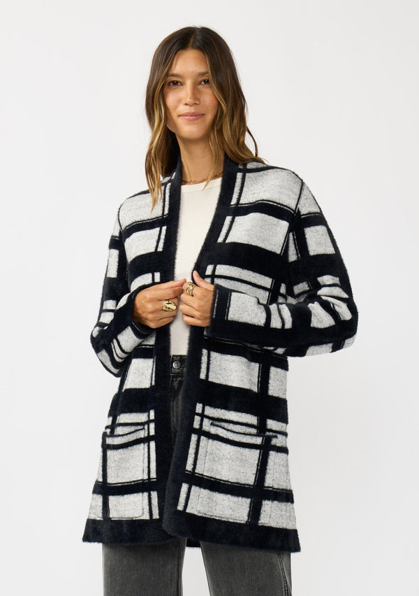 [Color: Black/Grey] A front facing image of a brunette model wearing a black and grey fuzzy plaid cardigan with an open front and patch pockets. A cozy cardigan for the fall season. 
