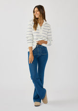 [Color: White/Blue] A front facing image of a brunette model wearing a white and blue striped knit pullover sweater with a half zip front. 