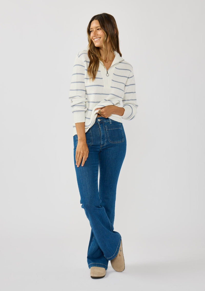 [Color: White/Blue] A front facing image of a brunette model wearing a white and blue striped knit pullover sweater with a half zip front. 