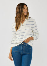 [Color: White/Blue] A front facing image of a brunette model wearing a white and blue striped knit pullover sweater with a half zip front. 