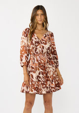 [Color: Nude/Brown] A front facing image of a brunette model wearing a brown abstract print mini dress with a split v-neckline, smocked waist, and 3/4 length sleeves. A fall boho mini dress for casual outings. 