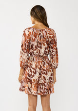 [Color: Nude/Brown] A back facing image of a brunette model wearing a brown abstract print mini dress with a split v-neckline, smocked waist, and 3/4 length sleeves. A fall boho mini dress for casual outings. 