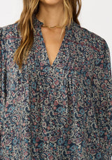 [Color: Navy/Rose] A detail image of a brunette model wearing a navy floral blouse with 3/4 length sleeves, a split v-neckline, and front pintuck details. A classic boho blouse for casual outings. 