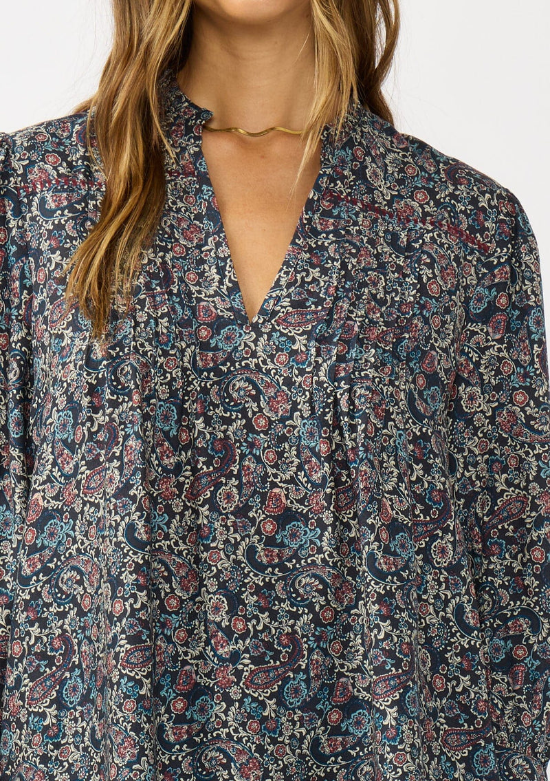 [Color: Navy/Rose] A detail image of a brunette model wearing a navy floral blouse with 3/4 length sleeves, a split v-neckline, and front pintuck details. A classic boho blouse for casual outings. 