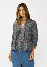 [Color: Navy/Rose] A front facing image of a brunette model wearing a navy floral blouse with 3/4 length sleeves, a split v-neckline, and front pintuck details. A classic boho blouse for casual outings. 