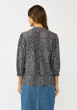 [Color: Navy/Rose] A back facing image of a brunette model wearing a navy floral blouse with 3/4 length sleeves, a split v-neckline, and front pintuck details. A classic boho blouse for casual outings. 