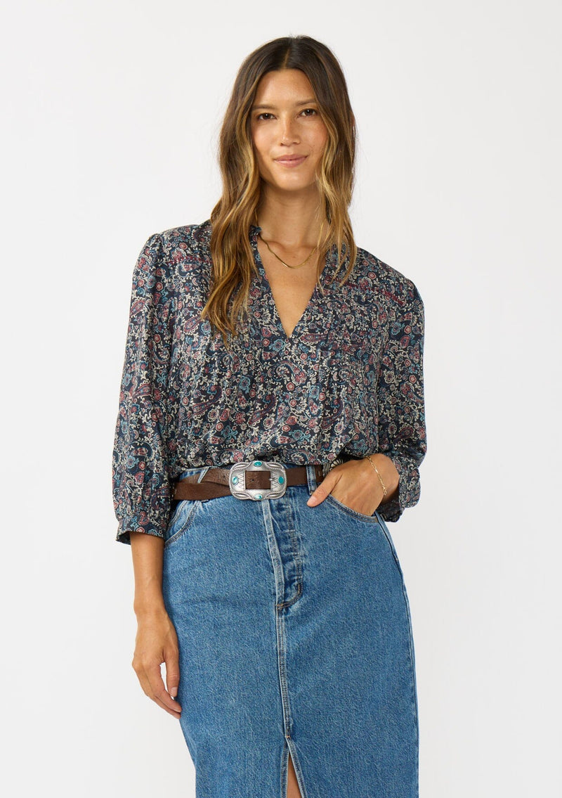 [Color: Navy/Rose] A front facing image of a brunette model wearing a navy floral blouse with 3/4 length sleeves, a split v-neckline, and front pintuck details. A classic boho blouse for casual outings. 