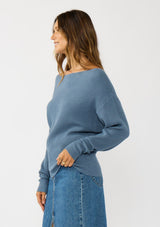 [Color: Cream] A side facing image of a brunette model wearing a blue waffle knit pullover sweater. With long sleeves, a relaxed fit, and a wide neckline that can be worn off the shoulder.
