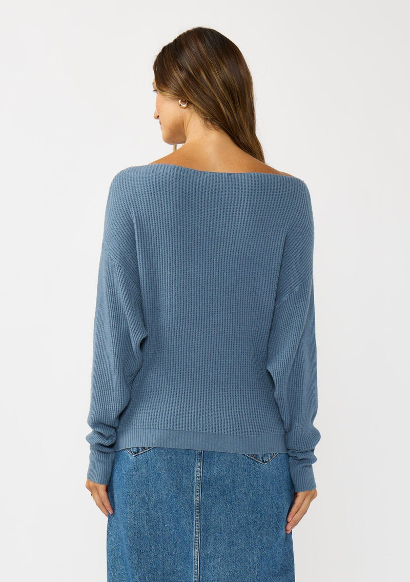 [Color: Cream] A back facing image of a brunette model wearing a blue waffle knit pullover sweater. With long sleeves, a relaxed fit, and a wide neckline that can be worn off the shoulder.