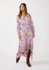 [Color: Natural/Dusty Blue] A front facing image of a brunette model wearing a blue and pink floral maxi dress with long sleeves, a split v-neckline with ties, a smocked waist, and a side slit. 
