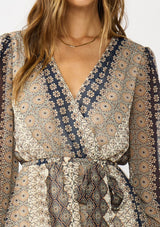 [Color: Natural/Navy] A detail image of a brunette model wearing a striped floral pattern mini dress with long sleeves, a surplice v-neckline, and an elastic waist with tie detail. A casual fall boho dress for brunch and special occasions. 