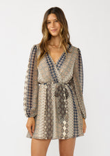 [Color: Natural/Navy] A front facing image of a brunette model wearing a striped floral pattern mini dress with long sleeves, a surplice v-neckline, and an elastic waist with tie detail. A casual fall boho dress for brunch and special occasions. 