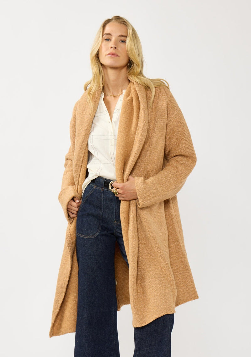 [Color: Camel] A front facing image of a blonde model wearing a best selling oversized cardigan in a camel brown color. A cozy and thick sweater coat with a hood, an open front, side pockets, a cocoon style silhouette, and a mid length hem. 