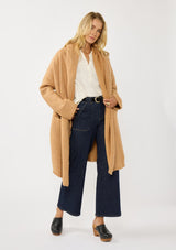 [Color: Camel] A front facing image of a blonde model wearing a best selling oversized cardigan in a camel brown color. A cozy and thick sweater coat with a hood, an open front, side pockets, a cocoon style silhouette, and a mid length hem. 