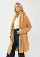 [Color: Camel] A side facing image of a blonde model wearing a best selling oversized cardigan in a camel brown color. A cozy and thick sweater coat with a hood, an open front, side pockets, a cocoon style silhouette, and a mid length hem. 