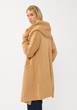 [Color: Camel] A back facing image of a blonde model wearing a best selling oversized cardigan in a camel brown color. A cozy and thick sweater coat with a hood, an open front, side pockets, a cocoon style silhouette, and a mid length hem. 