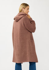 [Color: Vintage Mauve] A back facing image of a blonde model wearing a best selling oversized cardigan in a mauve color. A cozy and thick sweater coat with a hood, an open front, side pockets, a cocoon style silhouette, and a mid length hem. 