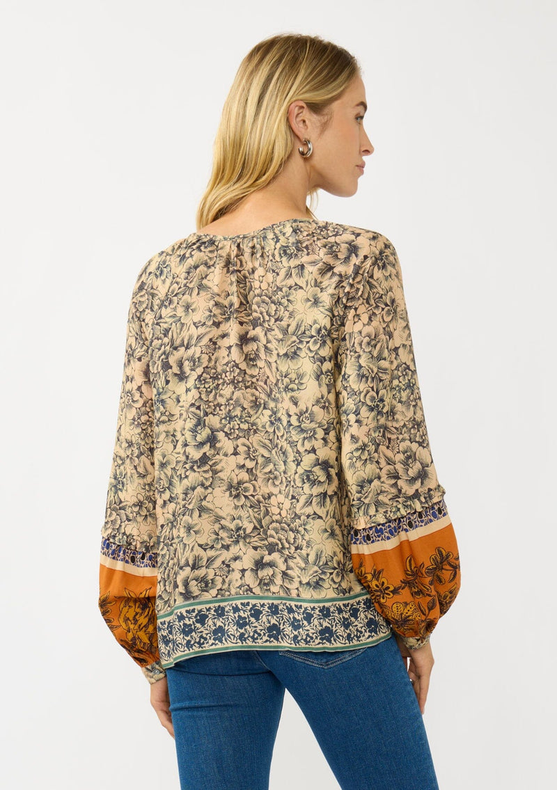 [Color: Natural/Rust] A back facing image of a blonde model wearing a yellow and orange floral blouse with a split v-neckline and long voluminous sleeves. A stunning bohemian fall blouse.