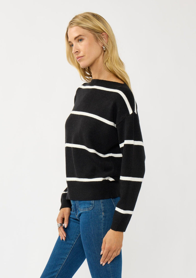 [Color: Black/White] A side facing image of a blonde model wearing a classic black and white striped knit pullover sweater. With long sleeves, a boat neckline, and ribbed trims. Perfectly relaxed and boxy for everyday styling. 