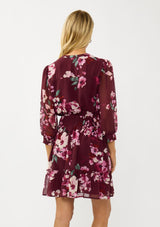 [Color: Wine/Dusty Rose] A back facing image of a blonde model wearing a burgundy floral mini dress with 3/4 sleeves, a smocked waist, button front, and a ruffle tiered skirt. 