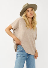 [Color: Heather Light Taupe] A front facing image of a blonde model wearing a light brown sweater dop with short dolman sleeves and a v-neckline. Effortless and cozy for cold weather outings. 