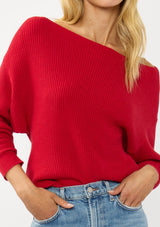[Color: Red] A detail image of a blonde model wearing a red waffle knit pullover sweater. With long sleeves, a relaxed fit, and a wide neckline that can be worn off the shoulder.