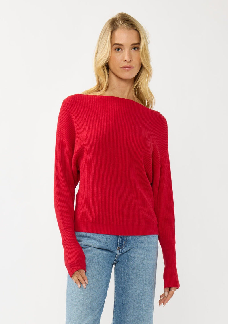 [Color: Red] A front facing image of a blonde model wearing a red waffle knit pullover sweater. With long sleeves, a relaxed fit, and a wide neckline that can be worn off the shoulder.