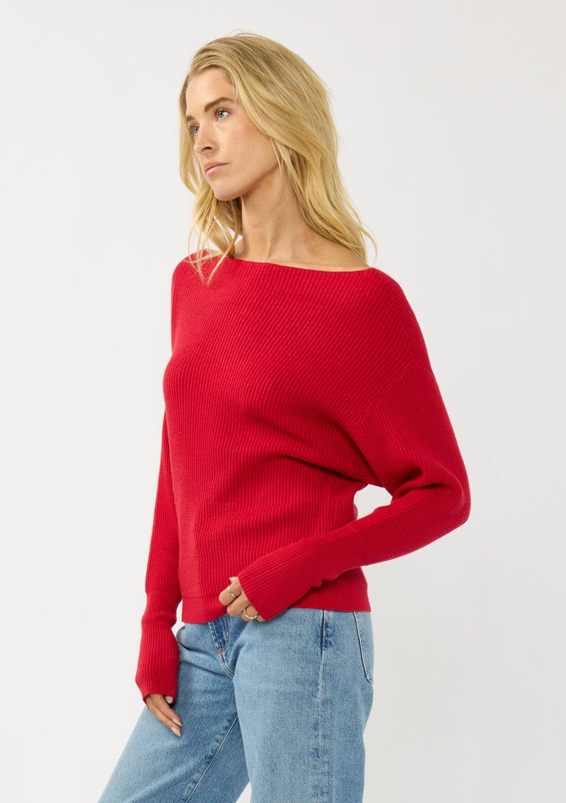 [Color: Red] A side facing image of a blonde model wearing a red waffle knit pullover sweater. With long sleeves, a relaxed fit, and a wide neckline that can be worn off the shoulder.