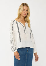 [Color: White/Black] A front facing image of a blonde model wearing a white cotton top with black embroidered details. A classic boho top with a split v-neckline, button front, and long sleeves.  