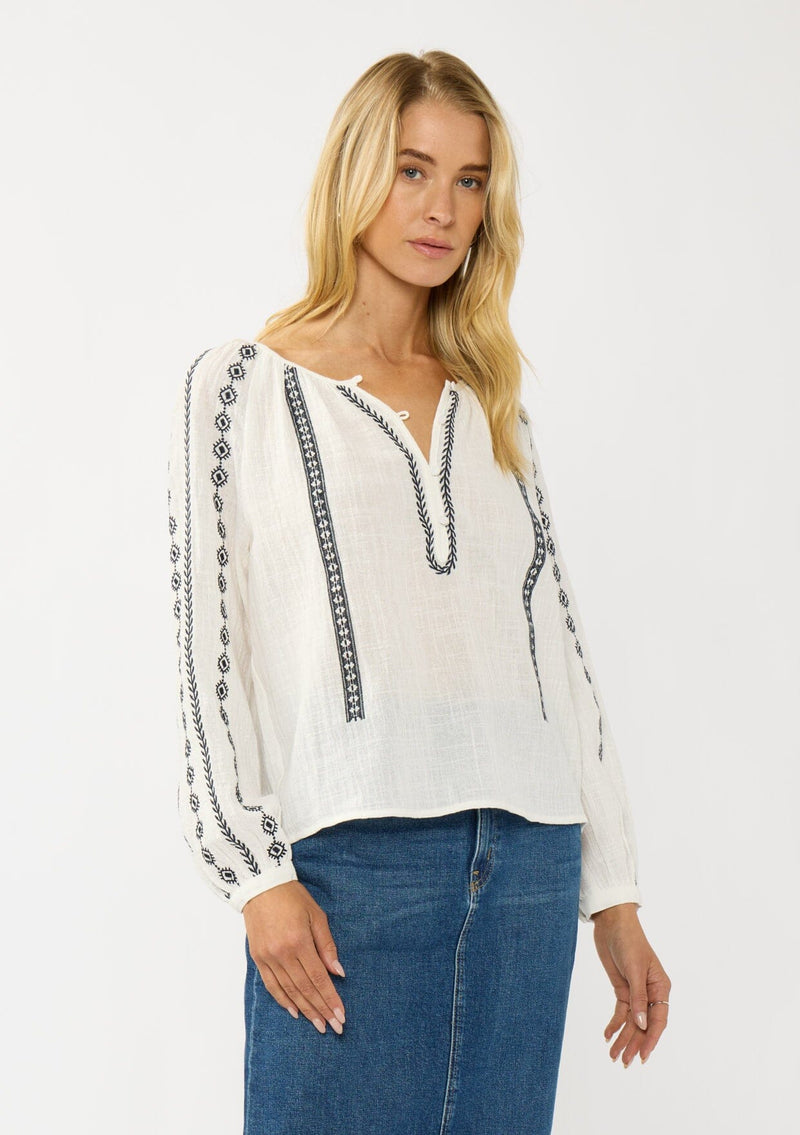 [Color: White/Black] A front facing image of a blonde model wearing a white cotton top with black embroidered details. A classic boho top with a split v-neckline, button front, and long sleeves.  